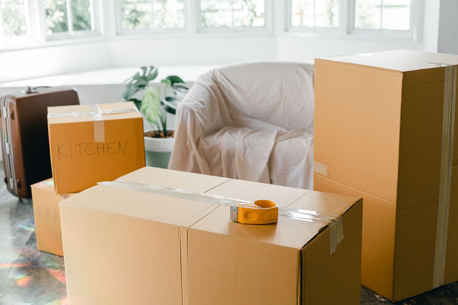 Packed moving boxes in a living room, with an armchair covered by a protective sheet.